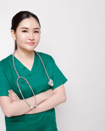 Portrait of a confident nurse in green scrubs with crossed arms and stethoscope, indoor studio setting.